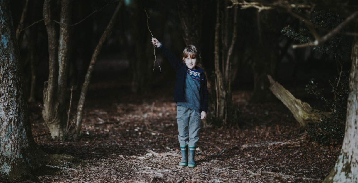 A boy in the woods at nighttime holding a stick in the air