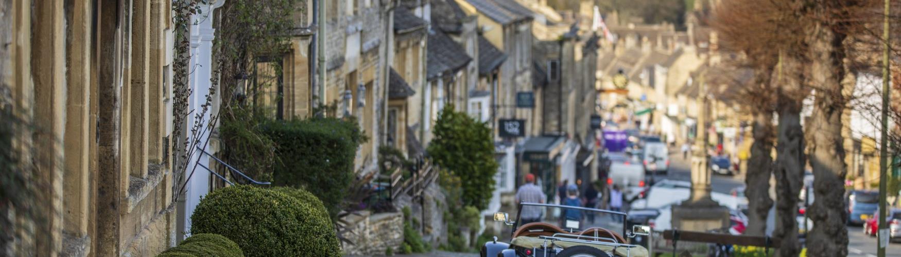 A classic car parked with Burford High Street in the distance